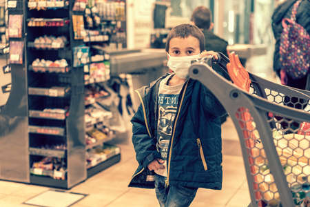 Boy wears protected mask in store. Shopping time during coronavirus outbreak. Boy in a medical mask. Shopping with kids during virus outbreak. Boy in face mask in supermarket. tonedの写真素材
