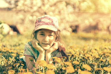 Closeup portrait of little cute girl lying with dandelions on the grass. Happy smiling girl lies on the grass among yellow flowering dandelions in the park. tonedの写真素材
