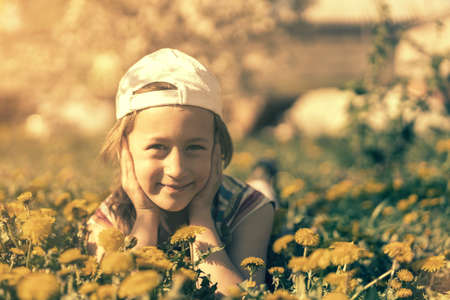 Closeup portrait of little cute girl lying with dandelions on the grass. Happy smiling girl lies on the grass among yellow flowering dandelions in the park. tonedの写真素材
