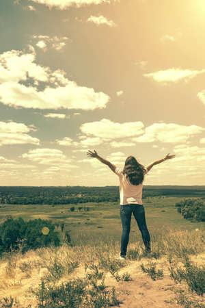 Young woman standing in a wheat field with sunrise on the background. A view from the back of a women standing on a mountain and admires the beautiful view sunset. tonedの写真素材