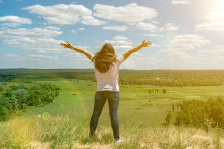Young woman standing in a wheat field with sunrise on the background. A view from the back of a women standing on a mountain and admires the beautiful view sunset. tonedの写真素材