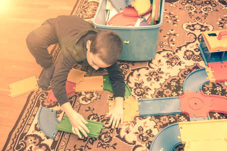 charming boy plays on the floor with car track. Child playing with toys indoor. Activities for kids at home. toddler activities. Kindergarten boy at home during quarantine. tonedの写真素材