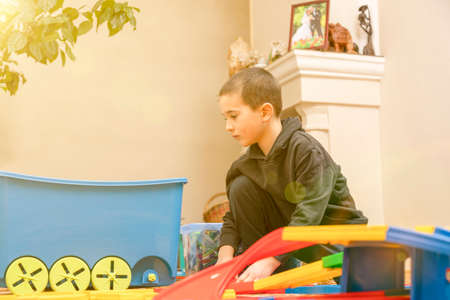 charming boy plays on the floor with car track. Child playing with toys indoor. Activities for kids at home. toddler activities. Kindergarten boy at home during quarantine. tonedの写真素材