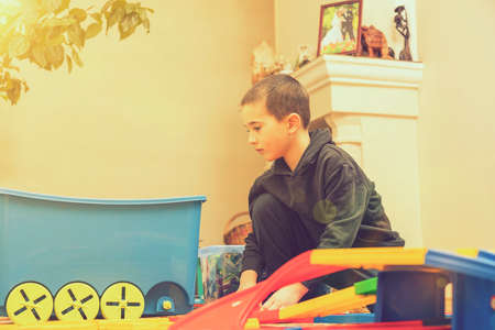 charming boy plays on the floor with car track. Child playing with toys indoor. Activities for kids at home. toddler activities. Kindergarten boy at home during quarantine. tonedの写真素材