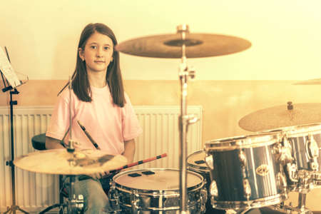 Happy girl in music therapy by playing drum kit on music room. Beautiful young girl drummer with drumsticks playing drums and cymbals. Female drummer. tonedの写真素材