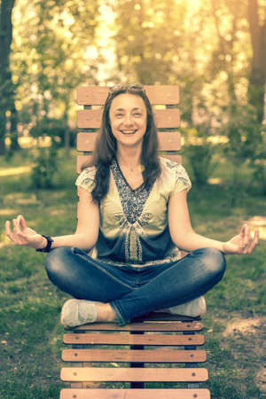 smile girl doing yoga and meditating in the city park on a sunny day. Sitting on a wooden bench. tonedの写真素材