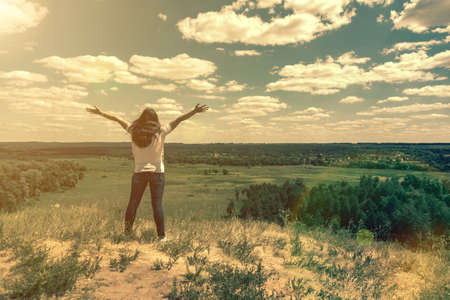 Young woman standing in a wheat field with sunrise on the background. A view from the back of a women standing on a mountain and admires the beautiful view sunset. tonedの写真素材
