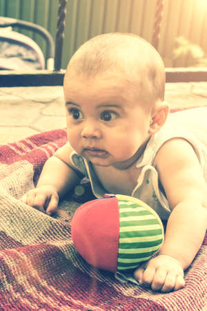 Adorable baby boy learning to crawl and playing with colorful rainbow ball toy. Cute laughing child crawling on a play mat. Nursery, clothing and toys for little kids. tonedの写真素材