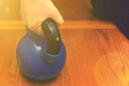 Iron kettlebell in the mans hand on a wooden background. Close up. Sports kettlebell in the gym, top view. kettlebells on gym. Close up. Sports kettlebell in the gym, top view. tonedの写真素材