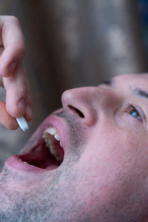 Extreme closeup man face taking white pill, mouth view swallowing pills, illness. man take medicine,open mouth and bring medicine to mouth. toned. selected focusの写真素材