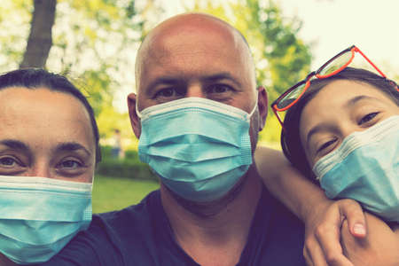 Family in protective medical masks. Mother, father, daughter protect themselves from the virus Coronavirus. Family in medical masks outdoors. close up. tonedの写真素材