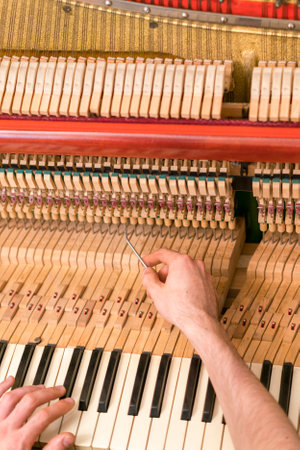Piano tuning process. closeup of hand and tools of tuner working on grand piano. Detailed view of Upright Piano during a tuning. toned. vertical photo. tonedの写真素材
