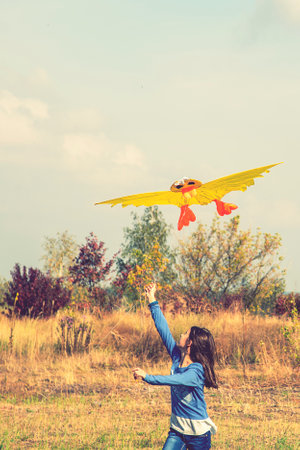 Teenage girl flying a yellow kite. Beautiful young girl kite fly. Happy little girl running with kite in hands on the beautiful field. vertical photo. tonedの写真素材