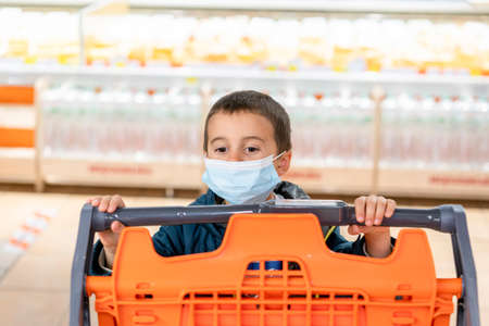 Boy wears protected mask in store. Shopping time during coronavirus outbreak. Boy in a medical mask. Shopping with kids during virus outbreak. Boy in face mask in supermarket. tonedの写真素材