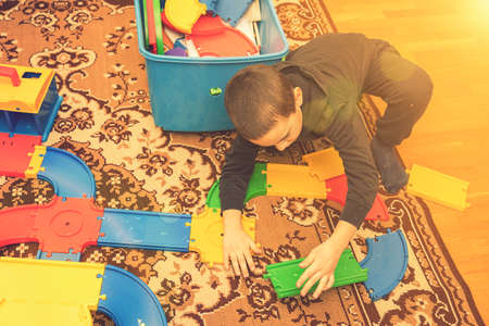 charming boy plays on the floor with car track. Child playing with toys indoor. Activities for kids at home. toddler activities. Kindergarten boy at home during quarantine. tonedの写真素材