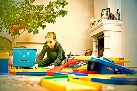 charming boy plays on the floor with car track. Child playing with toys indoor. Activities for kids at home. toddler activities. Kindergarten boy at home during quarantine. tonedの写真素材