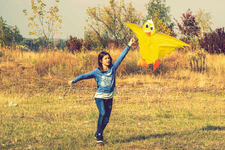 Teenage girl flying a yellow kite. Beautiful young girl kite fly. Happy little girl running with kite in hands on the beautiful field. vertical photo. tonedの写真素材