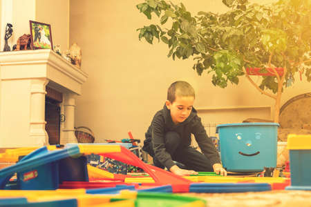 charming boy plays on the floor with car track. Child playing with toys indoor. Activities for kids at home. toddler activities. Kindergarten boy at home during quarantine. tonedの写真素材