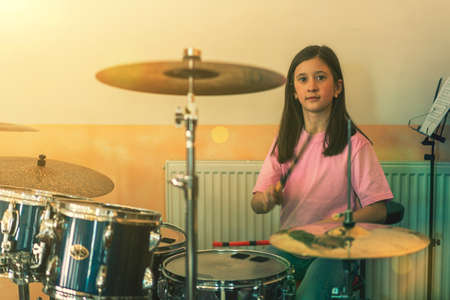 Happy girl in music therapy by playing drum kit on music room. Beautiful young girl drummer with drumsticks playing drums and cymbals. Female drummer. tonedの写真素材