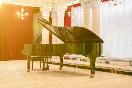 Grand Piano in Concert Hall. Piano standing on empty stage. opened black grand piano with stool on a wooden concert stage. tonedの写真素材
