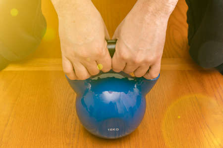 Iron kettlebell in the mans hand on a wooden background. Close up. Sports kettlebell in the gym, top view. kettlebells on gym. Close up. Sports kettlebell in the gym, top view. tonedの写真素材