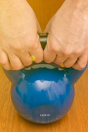 Iron kettlebell in the mans hand on a wooden background. Close up. Sports kettlebell in the gym, top view. kettlebells on gym. Close up. Sports kettlebell in the gym, top view. tonedの写真素材