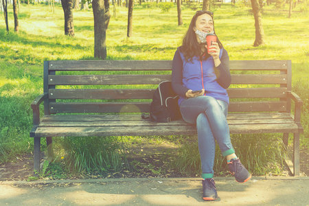 Beautiful Caucasian woman with long brown hair sitting on a yoga mat in the park drinking a cup of tea or coffee and smiling. Middle-aged athletic woman with long hair drinks coffee in a park. tonedの写真素材