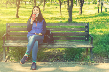 Beautiful Caucasian woman with long brown hair sitting in the park drinking a cup of tea or coffee and smiling. Middle-aged athletic woman with long hair drinks coffee in a park. tonedの写真素材