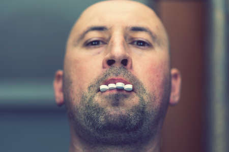 close-up portrait of man face mouth with pills between teet. Concept of taking number of medicationsの写真素材