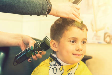 little boy having a haircut at hair salon..Children hairdresser with scissors and comb is cutting little boy. Contented cute preschooler boy getting the haircut. tonedの写真素材