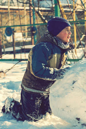boy sculpt a snowman in the backyard of the house clear winter day. The boy rolls a snowball to build a snowman in the yard during a heavy snowfall. tonedの写真素材