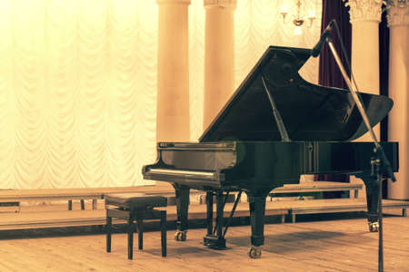 Grand Piano in Concert Hall. Piano standing on empty stage. opened black grand piano with stool on a wooden concert stage. tonedの写真素材