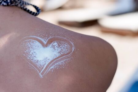 Heart made of sun cream is drawn on woman's shoulder at the beachの写真素材