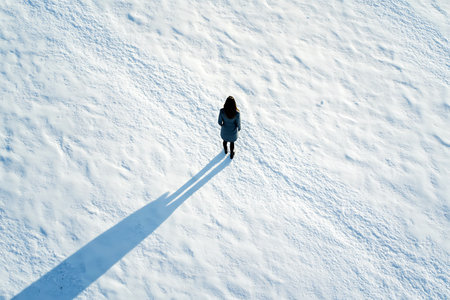 A solitary figure walks across a vast snow-covered landscape casting a long shadow in the winter sun.の写真素材