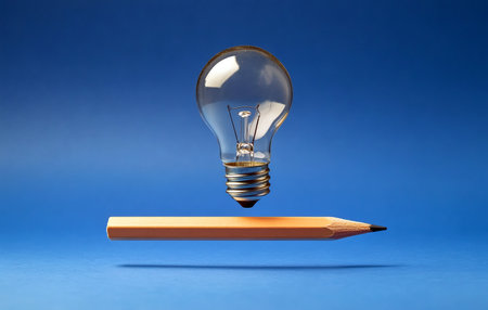 A lit lightbulb floats above a pencil on a bright blue background symbolizing ideas and creation.の写真素材
