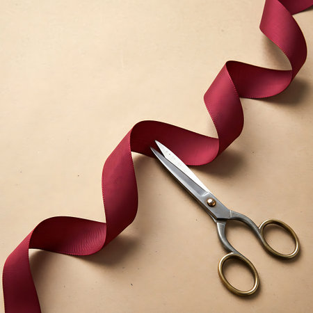 Scissors cutting red ribbon on a beige background, top viewの写真素材