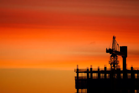 Silhouette of crane and building construction site at sunset time.