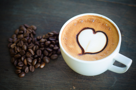 cup of coffee with latte art and heart coffee beans on wooden backgroundの写真素材