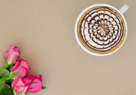 A cup of coffee with latte art and rose on brown paper backgroundの写真素材