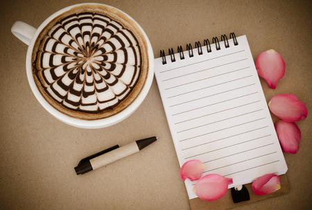 A cup of coffee with latte art and notebook on brown paper backgroundの写真素材