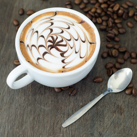 A cup of coffee with latte art and coffee bean on wooden backgroundの写真素材