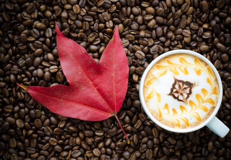 a cup of latte art and maple leaf on coffee bean backgroundの写真素材