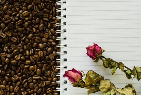 Notebook and wizened rose on coffee bean backgroundの写真素材