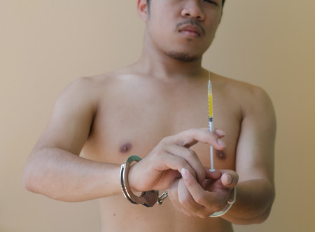 young man holding  syring in hand with handcuffsの写真素材