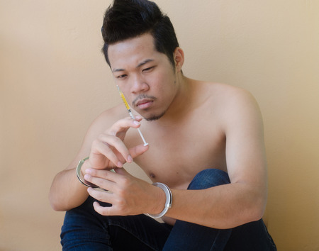 young man holding syringe in hand with handcuffsの写真素材