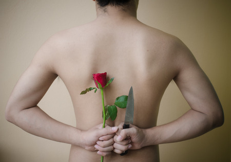 Picture a man holding a red rose and knife behind his backの写真素材