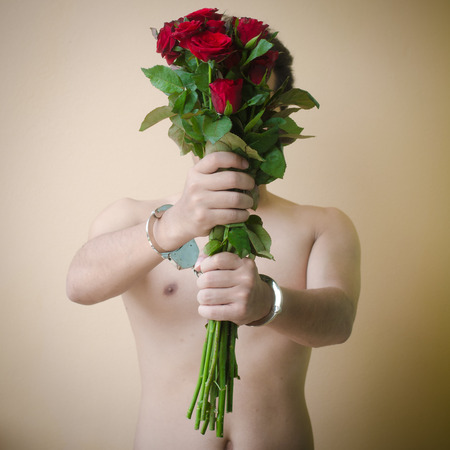 young man holding red rose in hand with handcuffsの写真素材