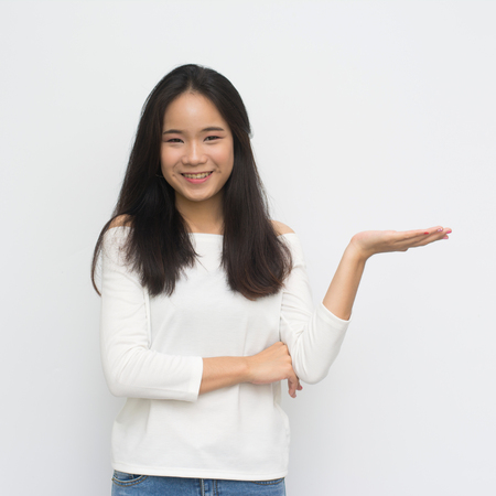 Asian girl shows a hand advertising. Woman with outstretched hand. Beautiful girl. Beautiful portrait of a girl in white shirt over a white background.の写真素材
