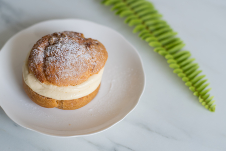 Profiterole or cream puff with filling and powdered sugar topping on white dishの写真素材