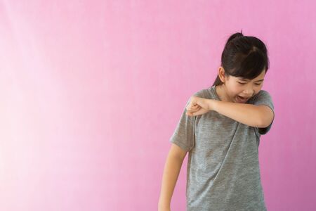 Little girl coughs in her elbow isolated on white background. Correct sneezing. Concept of stop spread of the virus. The girl covered her nose in her arm avoid air pollution, PM 2.5.の写真素材